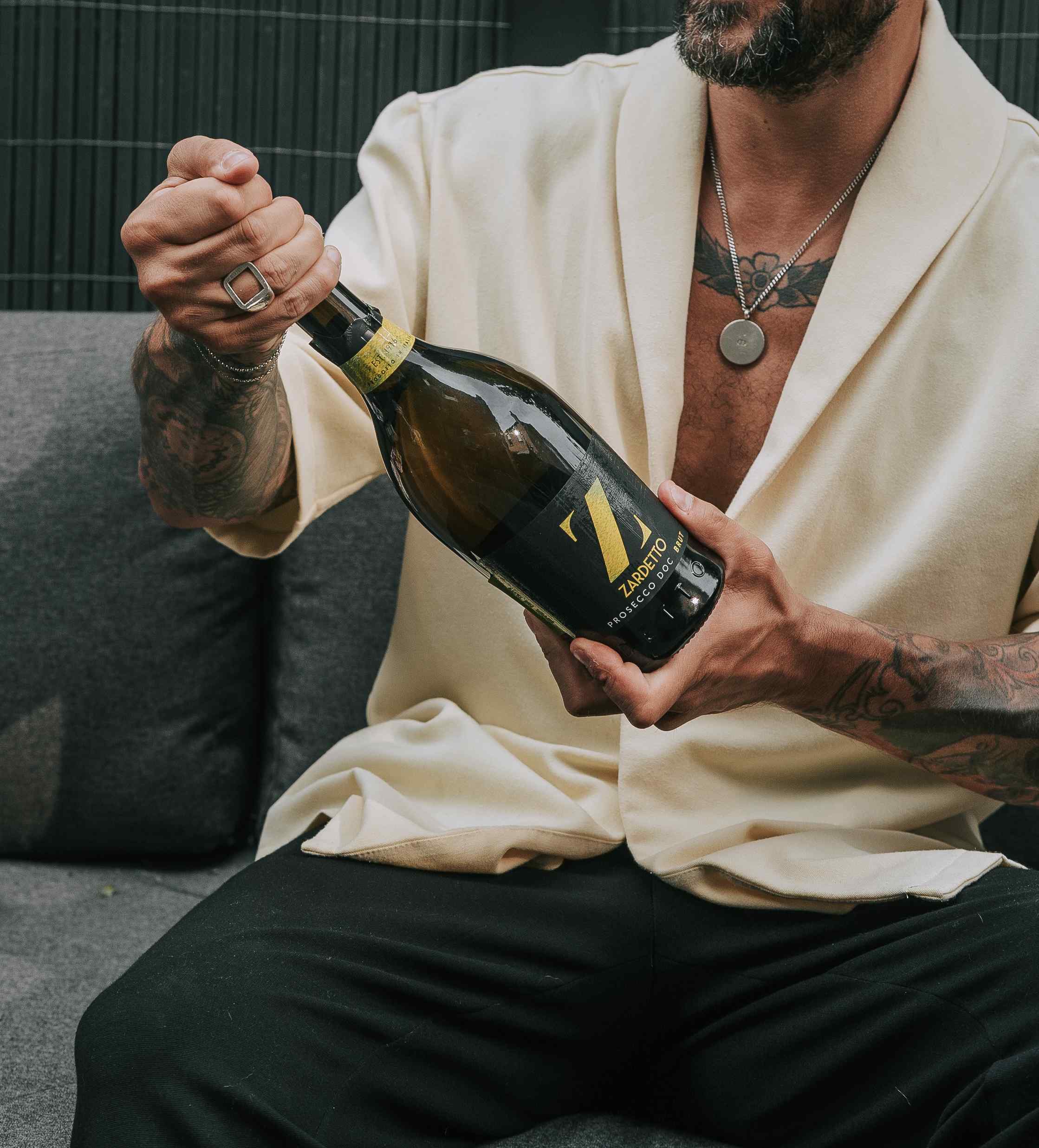 Man with tattooed arms opening a bottle of Zardetto prosecco, produced by Independent Non-Executive Directors at YesMore Drinks Marketing Consultancy