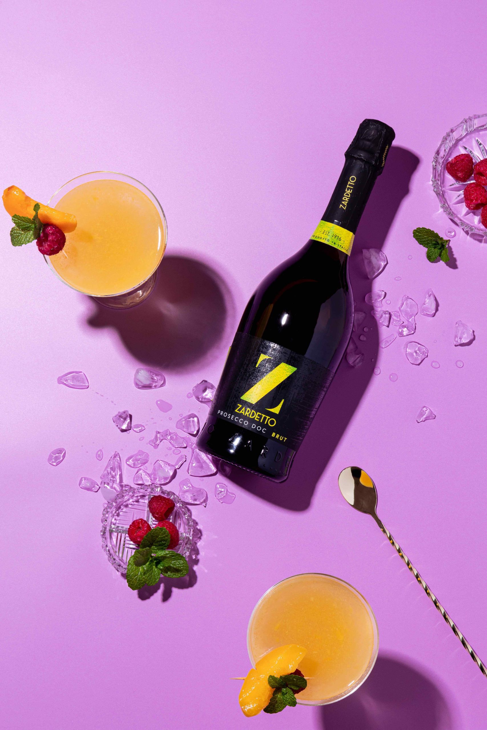 Bottle of Zardetto wine laying on a purple background with cocktails, produced by YesMore Wine Marketing Consultancy