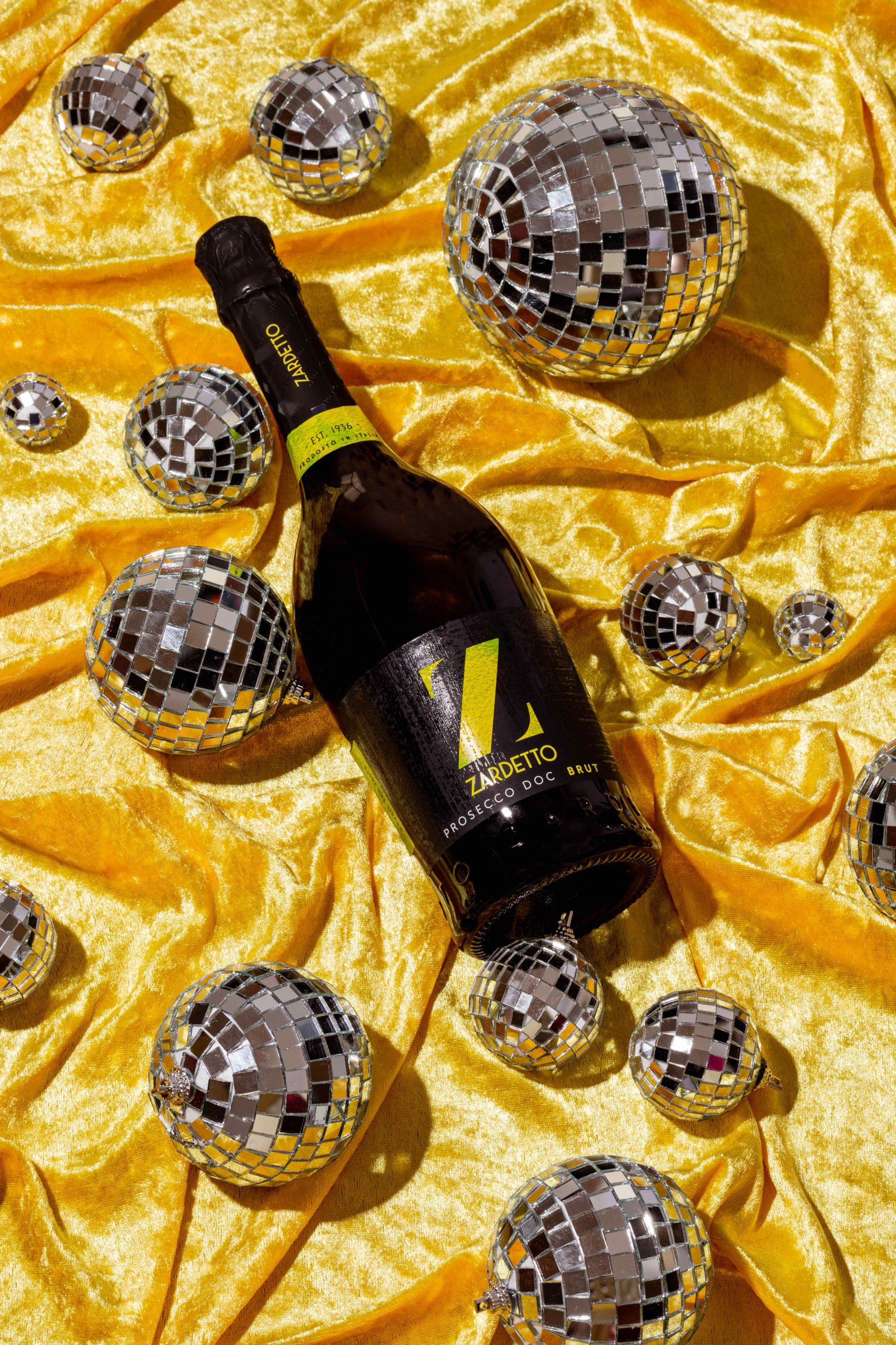 Bottle of Zardetto Prosecco laying on a yellow cloth surrounded in disco balls, produced by YesMore Wine Digital Marketing Agency